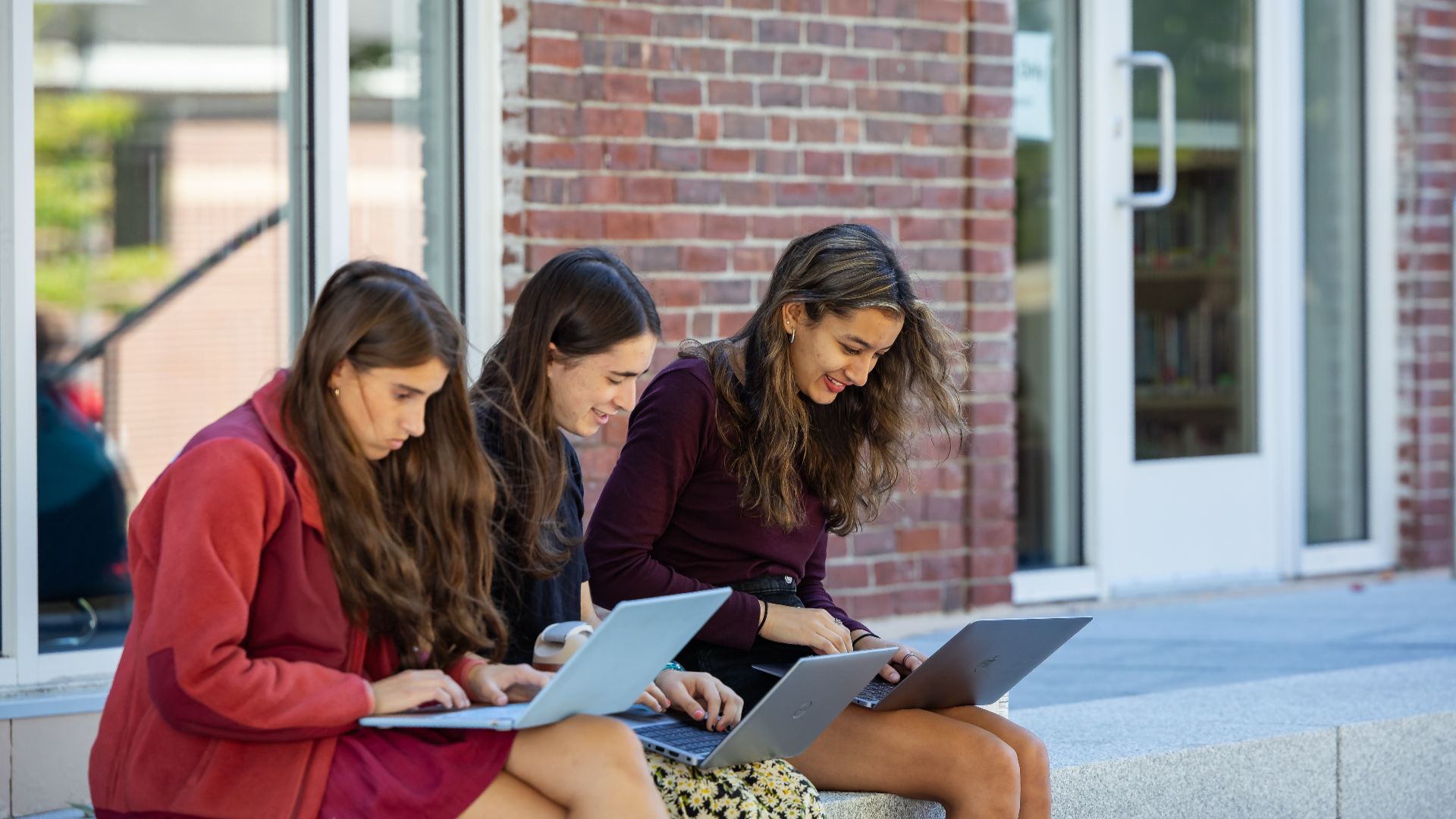 Three students sitting outdoors working on their laptops together