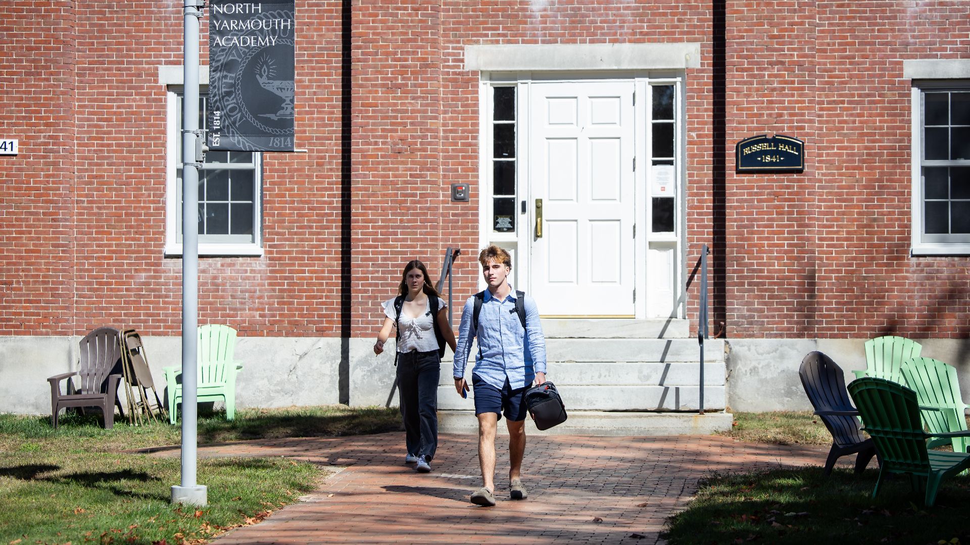 Two students walking along a brick path in front of a school building