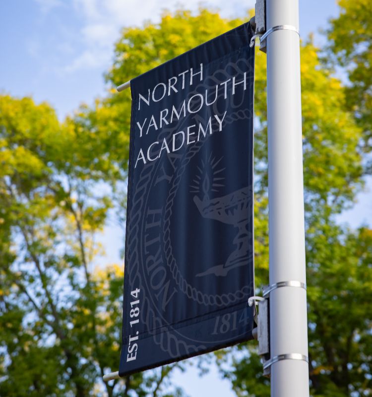 NYA banner hanging on a lamp post with trees in the background