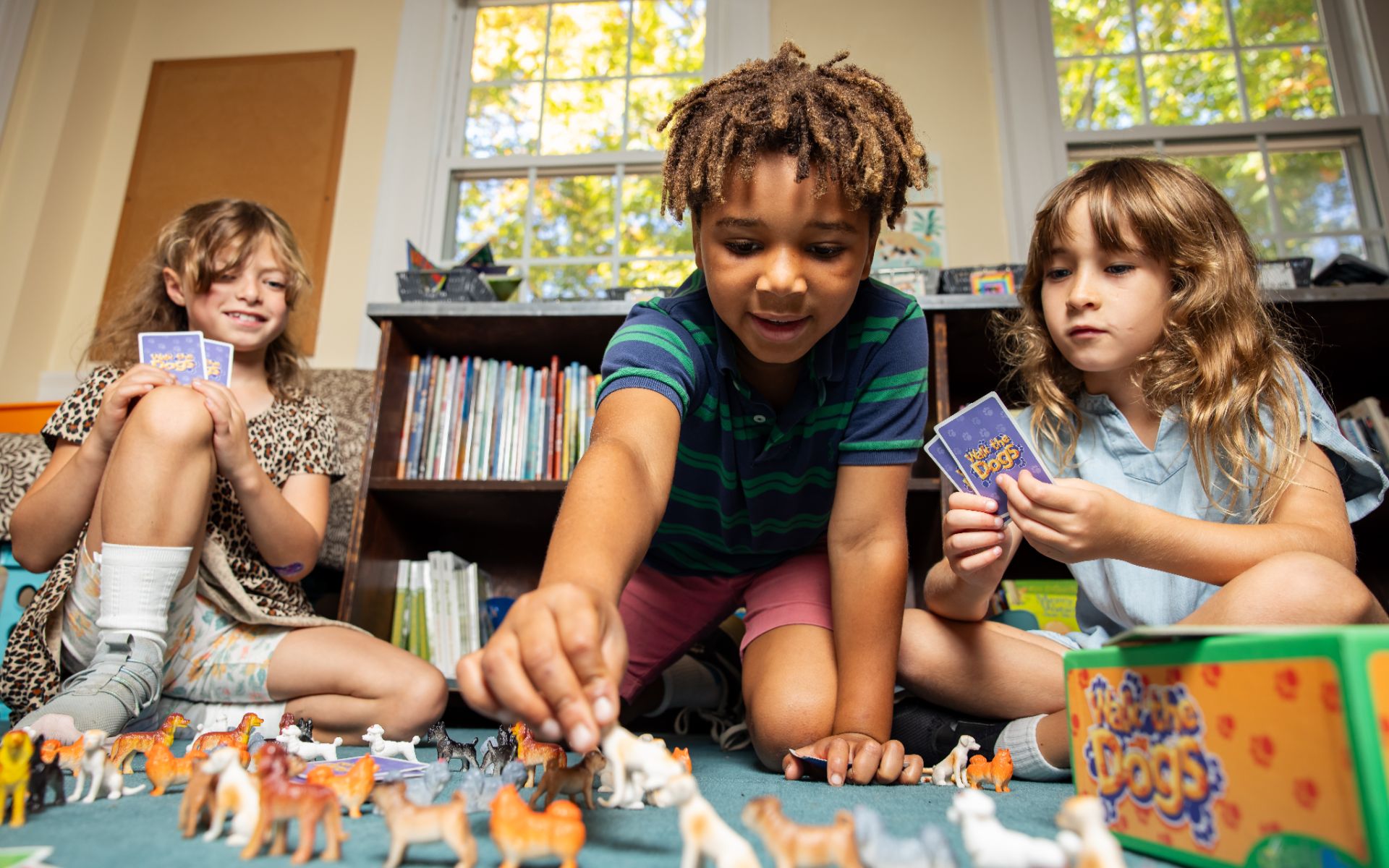 Three young children playing a dog-themed board game on a classroom floor