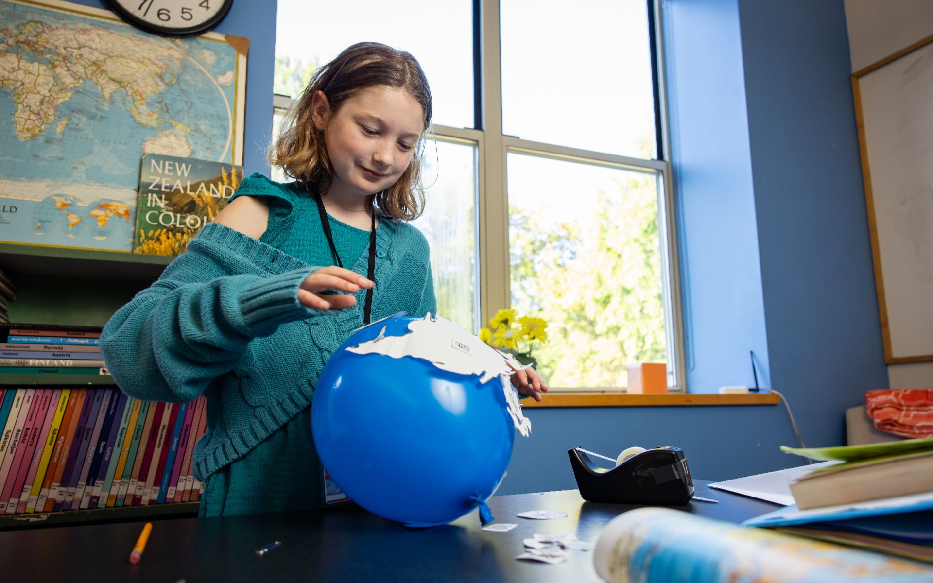 Student creating a globe model using a blue balloon in a classroom