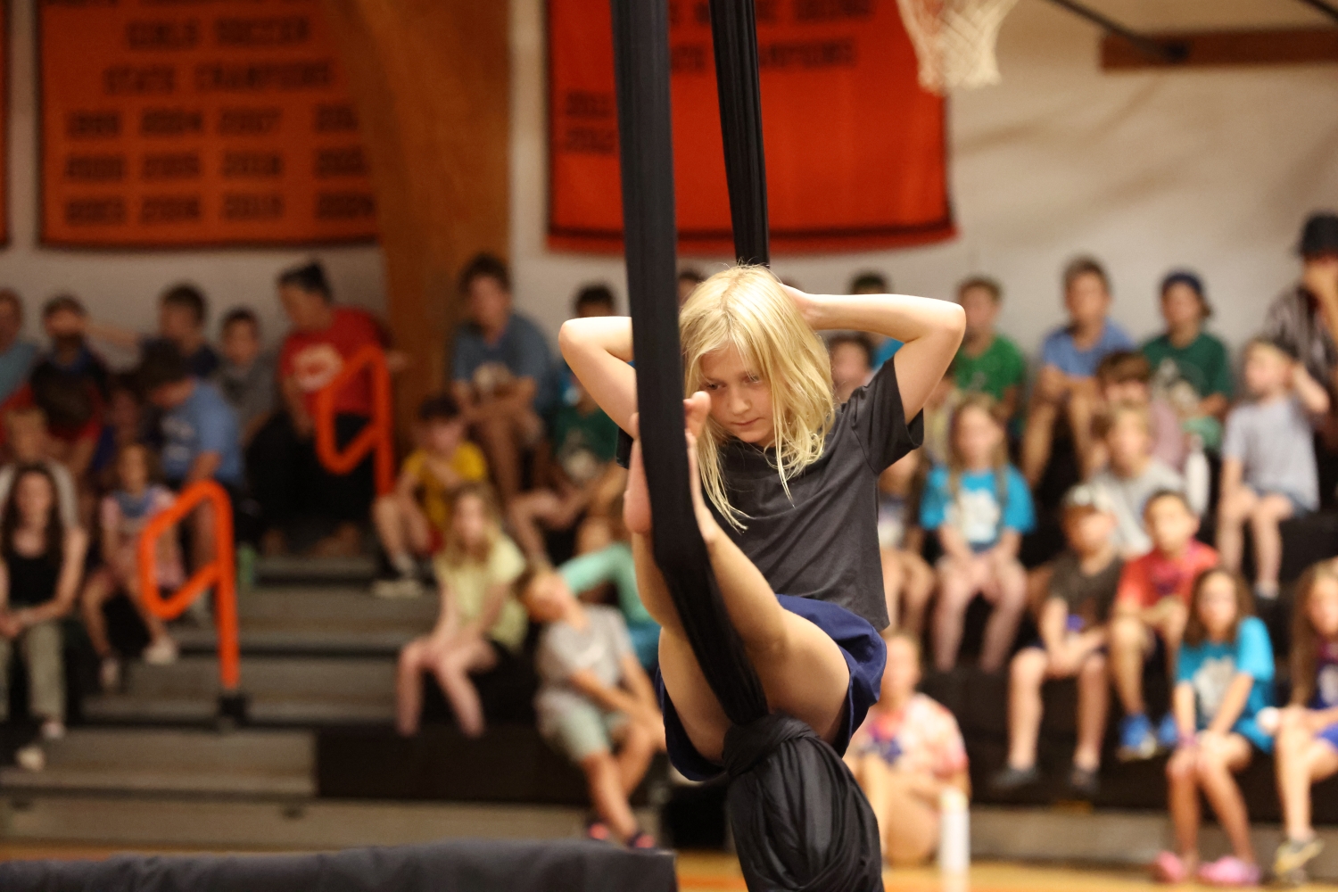A student performing an aerial silks routine in a school gymnasium